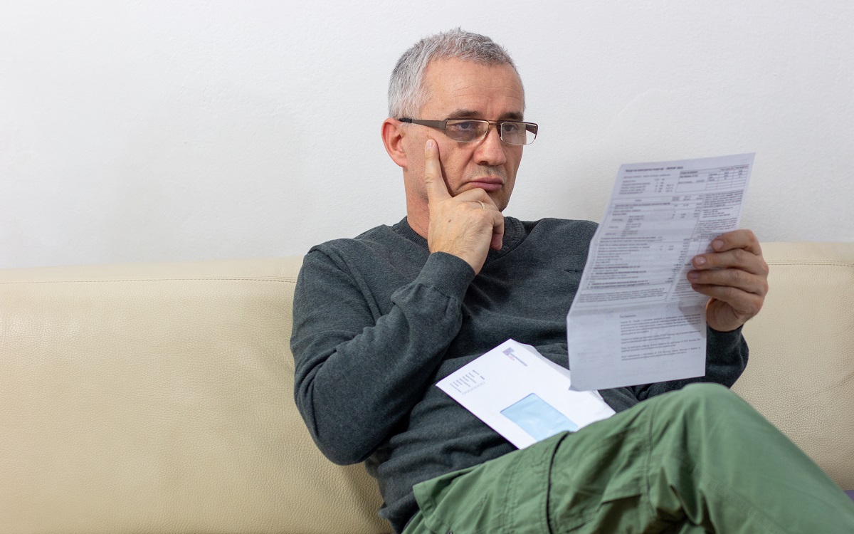 Worried   middle-aged man reading unexpected news in paper document. He is confused and astonished by unbelievable news: high bill tax invoice, debt notification, bad financial report, money problem